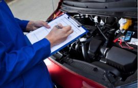 Image of a qualified mechanic looking under the bonnet of a car, writing the details out for a roadworthy certificate during an inspection